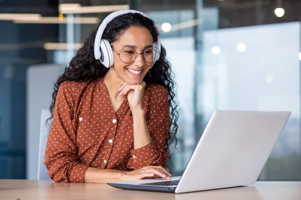 A woman wearing headphones working on a laptop inside an office or workplace.