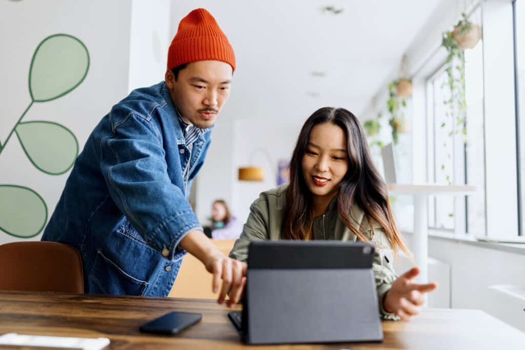 A man and woman are focused on a tablet screen, engaged in discussion.