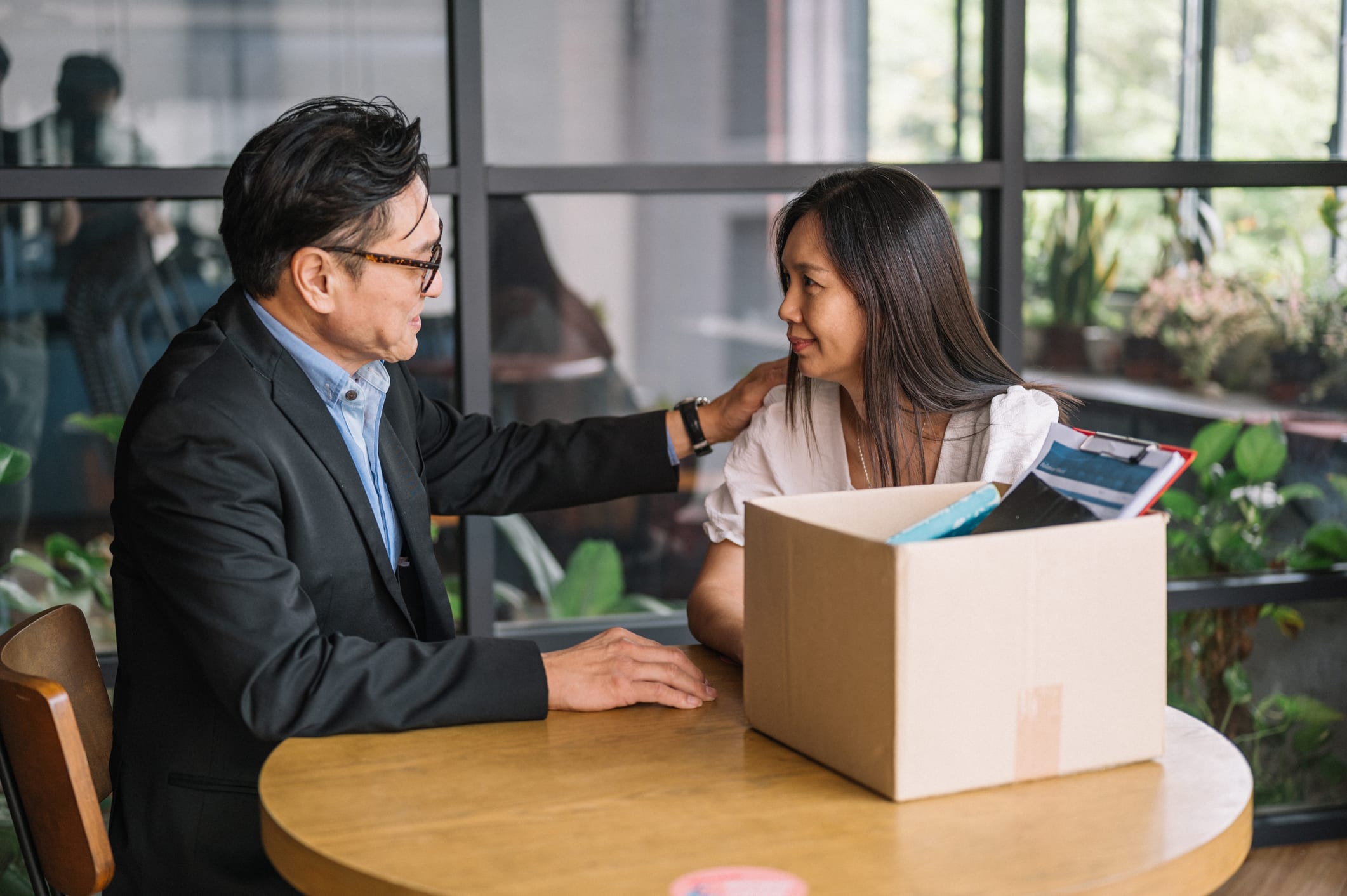 Employee packing belongings into a box, with a colleague offering support.