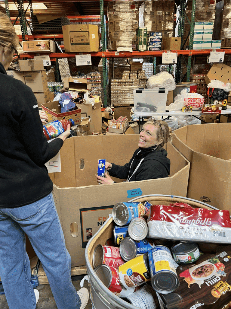 A person sitting in a large donation box, smiling and looking up at another person outside of the box.