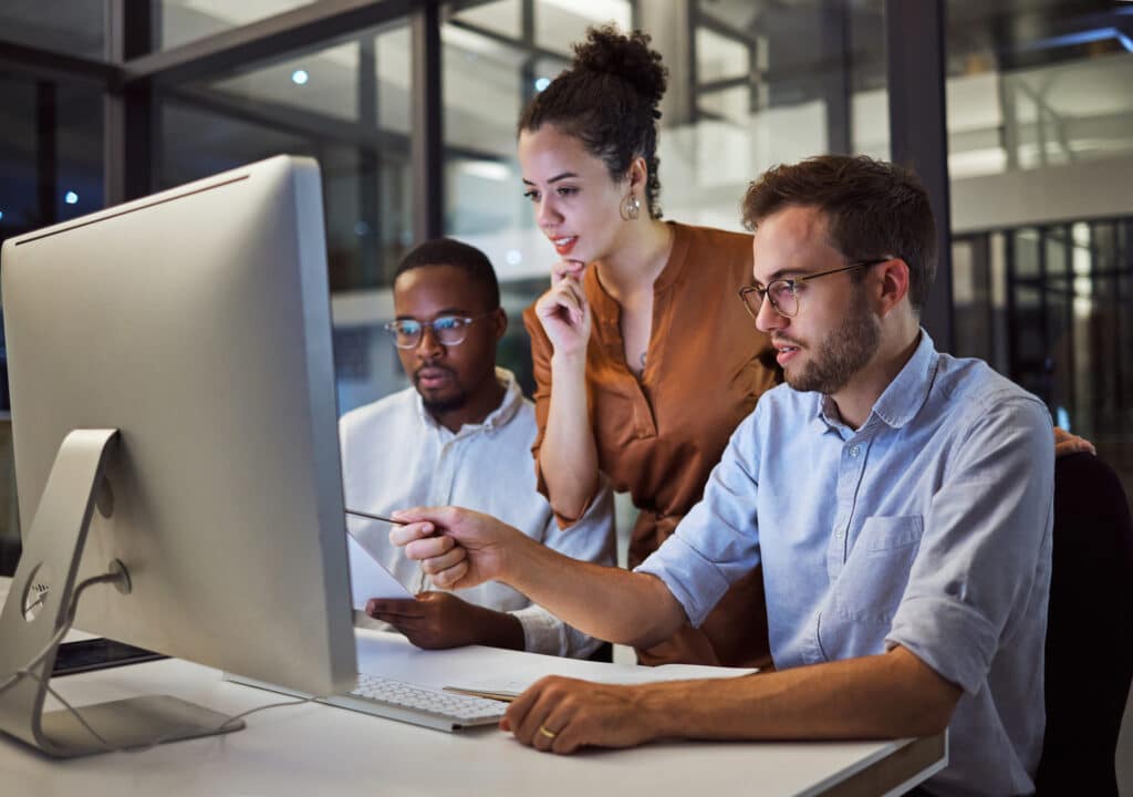 Three colleagues look at a computer and collaborate to solve a problem in a modern office.