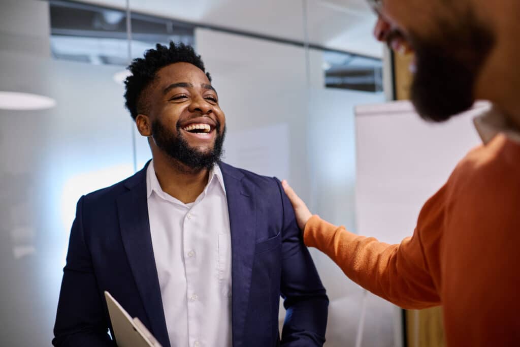 A male employee smiles at a colleague who’s speaking to him. The mood is warm and encouraging.