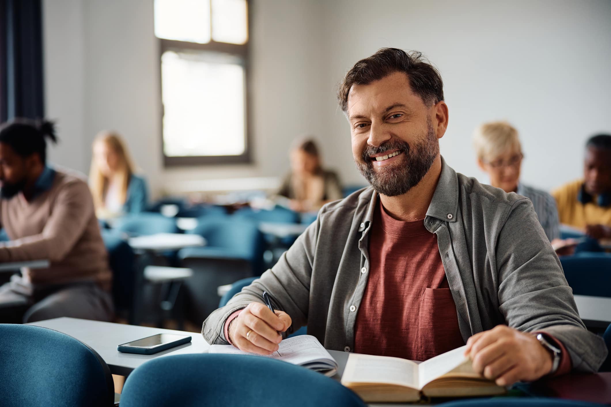 Smiling person sitting at a long desk in a classroom with other students working at desks around them