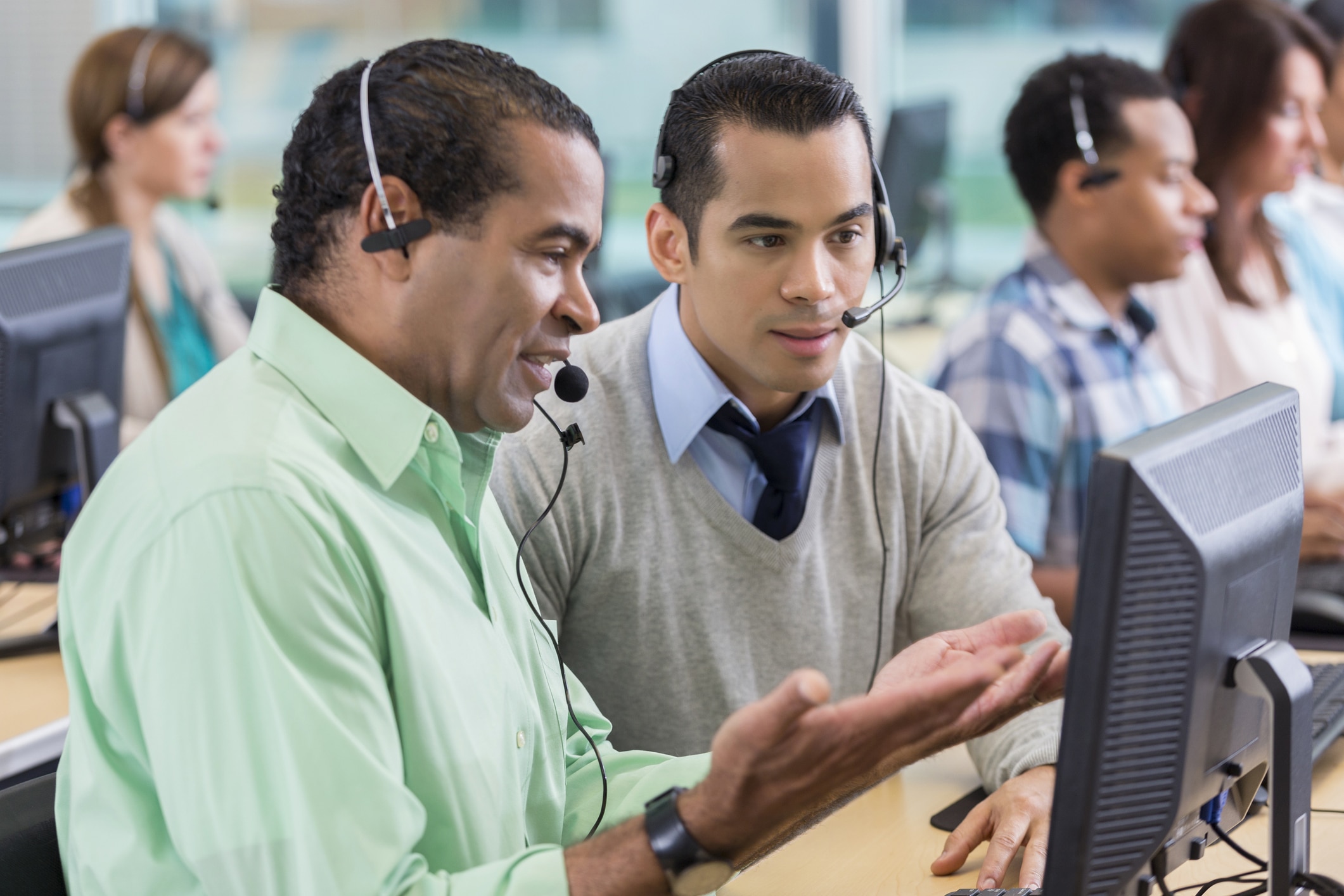 Helpful call center operator trains new employee using a computer
